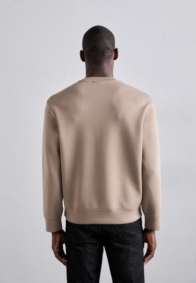 Beige genser med lange ermer og rund hals, med en glatt tekstur og ribbestrikket mansjetter; kombinert med mørk denimjeans.