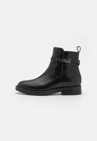Black leather ankle boot with a rounded toe, decorative strap with logo, and a low block heel. Smooth texture and minimalist design.