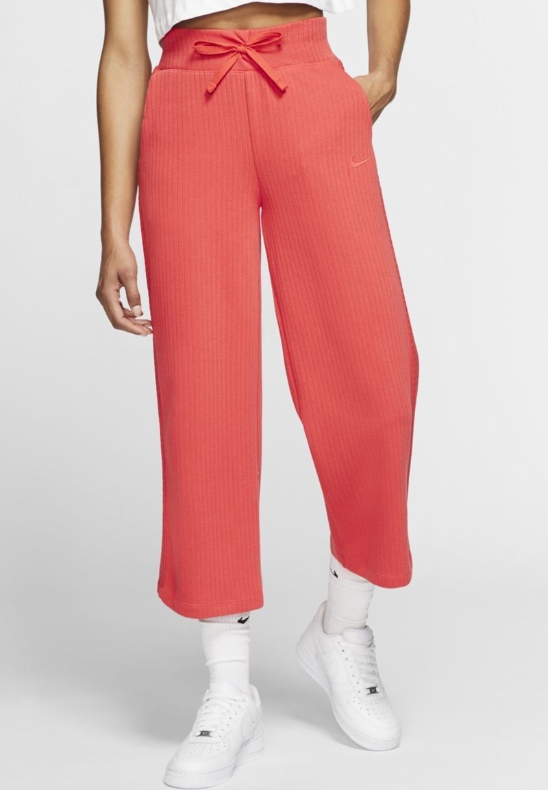 Röda ribbade vida byxor med dragsko i midjan, med en subtil Nike-logotyp. Bärs med vita sneakers och strumpor.