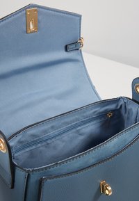 Borsa a mano in pelle blu con esterno liscio, ferrature dorate e tasca interna con cerniera. L'interno è foderato con tessuto azzurro chiaro.