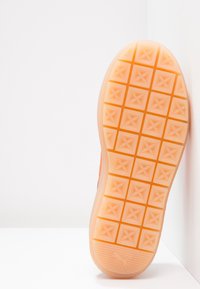 Semelle de chaussure présentant un motif à losanges, en caoutchouc orange, avec un bord lisse et un petit logo près de la base.