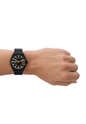 Schwarze sechseckige Uhr mit einem gold-weißen Ziffernblatt, Netzarmband und großen Ziffern. Auf einem Handgelenk mit einem natürlichen Hautton positioniert.