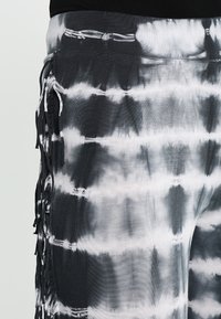 Joggers en tie-dye noir et blanc avec des franges sur les côtés, fabriqués en tissu doux, affichant une finition texturée.