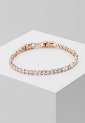 Tennisarmband aus Roségold mit klaren runden Kristallen in einer einzigen Reihe, dargestellt auf einem weißen Sockel vor grauem Hintergrund.