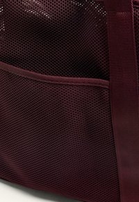 Burgundowa torba siatkowa z teksturowaną powierzchnią, z przednią kieszenią i mocnymi tkaninowymi uchwytami.