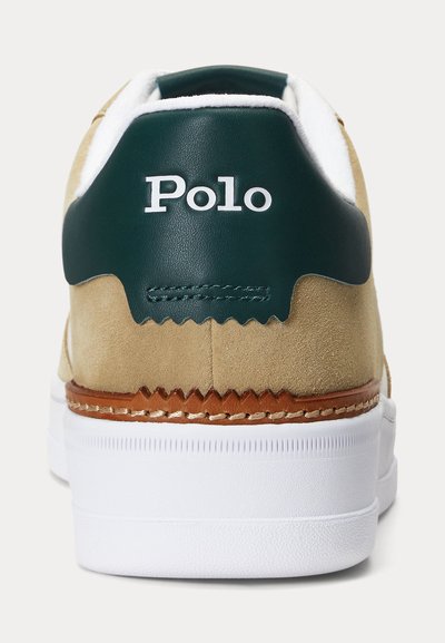 Beżowy zamszowy sneaker z białą podeszwą, ciemnozielonym skórzanym paskiem na pięcie i białym logo "Polo" umieszczonym centralnie na pięcie.