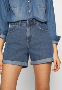 Jeansshorts med hög midja, med uppvikta ärmar, två framfickor och en blekt blå färg. Materialet är strukturerad denim.