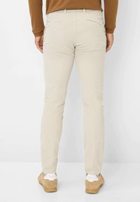 Beige corduroy broek met een rechte pasvorm, voorzien van twee achterzakken en subtiele stikseldetails. G gedragen met lichtbruine schoenen.