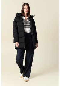 Abrigo tipo plumón negro con capucha, textura acolchada, cremallera frontal, llevado sobre una camiseta de rayas y pantalones de pierna ancha navy, combinado con zapatillas blancas.