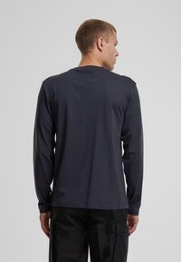 Långärmad t-shirt i mörkgrått tyg, enkel rundad halsdesign, slät textur, med en liten logoympning vid fållen.