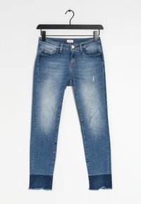 Štíhlé modré džíny z denimu se světlejšími místy, trhlinami a roztrhaným lemem. Obsahují klasické kapsy a kovové zapínání na knoflík v pase.