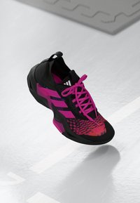 Svart atletisk sko med rosa detaljer, teksturert overdel og dristige mønstre. Har tre hvite striper og rosa snørebånd. Gummisåle.