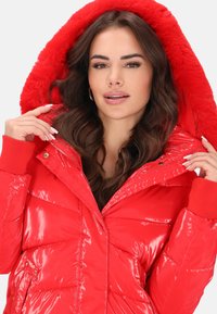 Piros, fényes felületű, puffadt dzseki műszőrme béléssel rendelkező kapucnival, bordázott mandzsettákkal és cipzáras első zsebekkel.