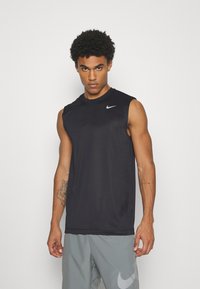 Sort ærmeløs Nike træningsskjorte med rund hals, lavet af glat stof; logo i hvidt på øverste venstre side; båret med grå shorts.