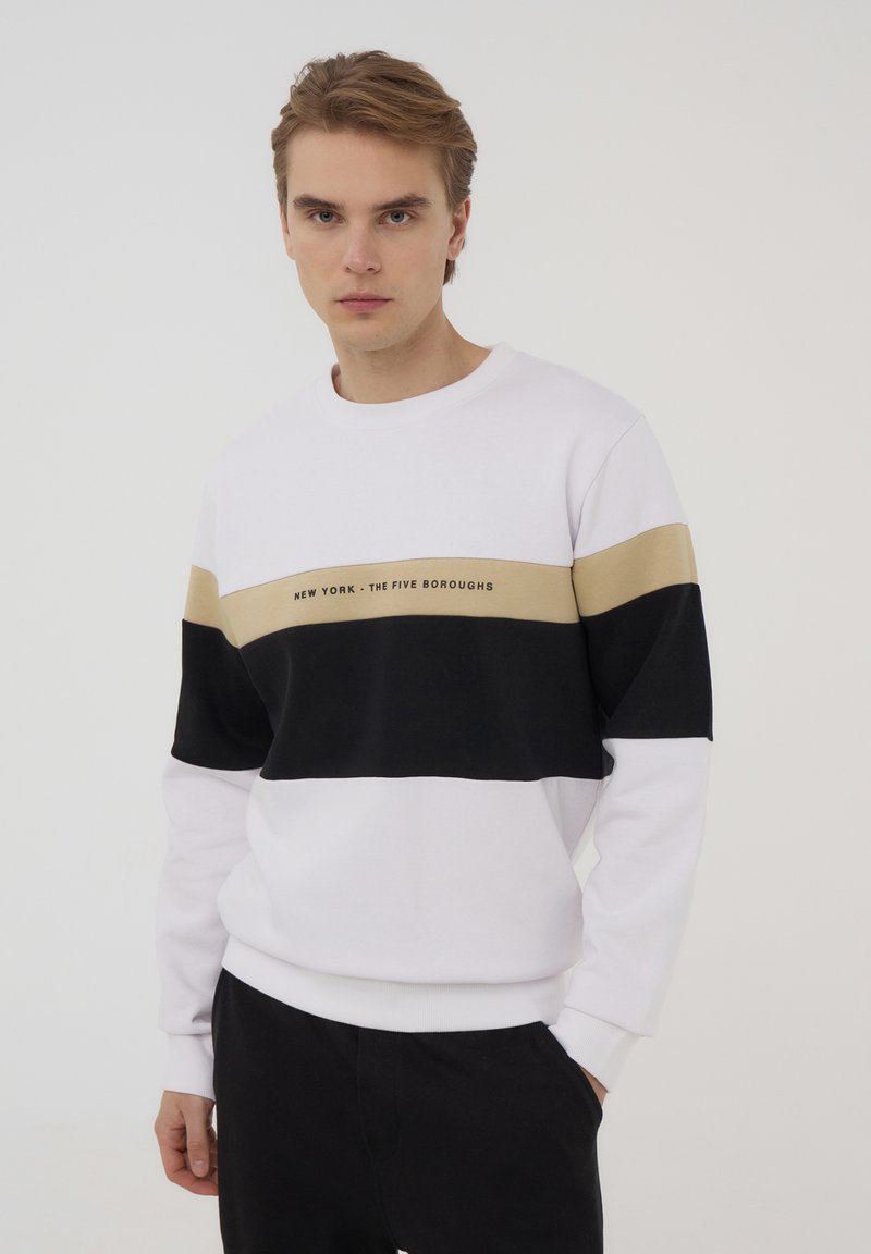 Felpa bianca con strisce orizzontali nere e beige, con testo "NEW YORK - THE FIVE BOROUGHS." Materiale morbido, vestibilità rilassata.