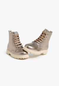 Metallisch goldene Knöchelstiefel mit beigen Gummisohlen, ausgestattet mit Schnürverschluss und strukturiertem Obermaterial. Knöchelhöhe mit Zuglasche an der Rückseite.