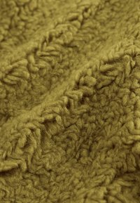 Približek tkanine v gorčično rumeni barvi z teksturiranim vzorcem kiti pletenine in mehko, puhasto vlakno.