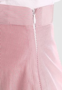 Jupe rayée rouge et blanche en tissu lisse, avec une taille ajustée et une fermeture éclair sur le côté avec une tirette blanche.