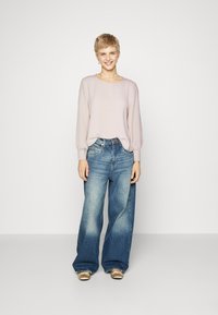 Light pink long-sleeve sweater and wide-leg denim jeans with a faded finish, accessorized with simple earrings and neutral-toned shoes.