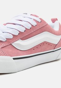 Baskets en daim rose avec des rayures blanches, des accents noirs et des lacets blancs. Surface texturée avec des perforations sur les côtés. Design à bout arrondi.