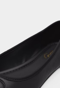 Gros plan sur une ballerine en cuir noir avec un bout arrondi et une couture discrète le long des bords.