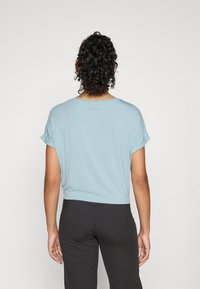Lysblå, cropped t-skjorte laget av mykt stoff, med rullede korte ermer og flat bakseam, kombinert med svarte leggings.