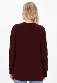 Maglione a trecce color bordeaux con maniche lunghe, scollo rotondo e polsini a coste. Un motivo testurizzato corre verticalmente lungo il capo.