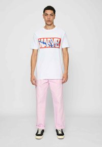 Hvid t-shirt med et farverigt "MARVEL" grafisk design, parret med lyserøde bukser og sorte sneakers med hvide såler.