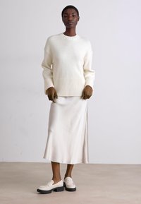 Cream ribbed sweater with a round neckline, paired with a satin cream midi skirt and chunky-soled white loafers. Smooth, soft texture.