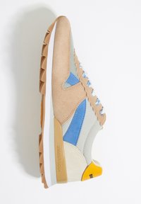 Zapatillas de ante beige con acentos en azul y amarillo, paneles de malla, superposiciones texturizadas y una suela de goma blanca con un dibujo de adherencia.