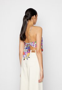 Top cropped com estampa floral multicolorida, com alças finas, atado nas costas, combinado com calças de cintura alta de cor creme.