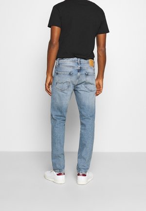 Jeans in denim blu sbiadito con taglio dritto, cinque tasche e una toppa in pelle marrone sulla vita posteriore. Abbinati a sneakers bianche.