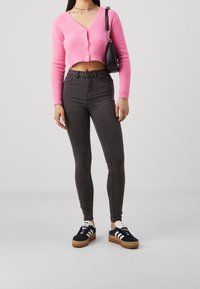 Rosa kort cardigan med knappar, tillsammans med hög midja mörkgrå skinny jeans och svarta sneakers med vita detaljer.