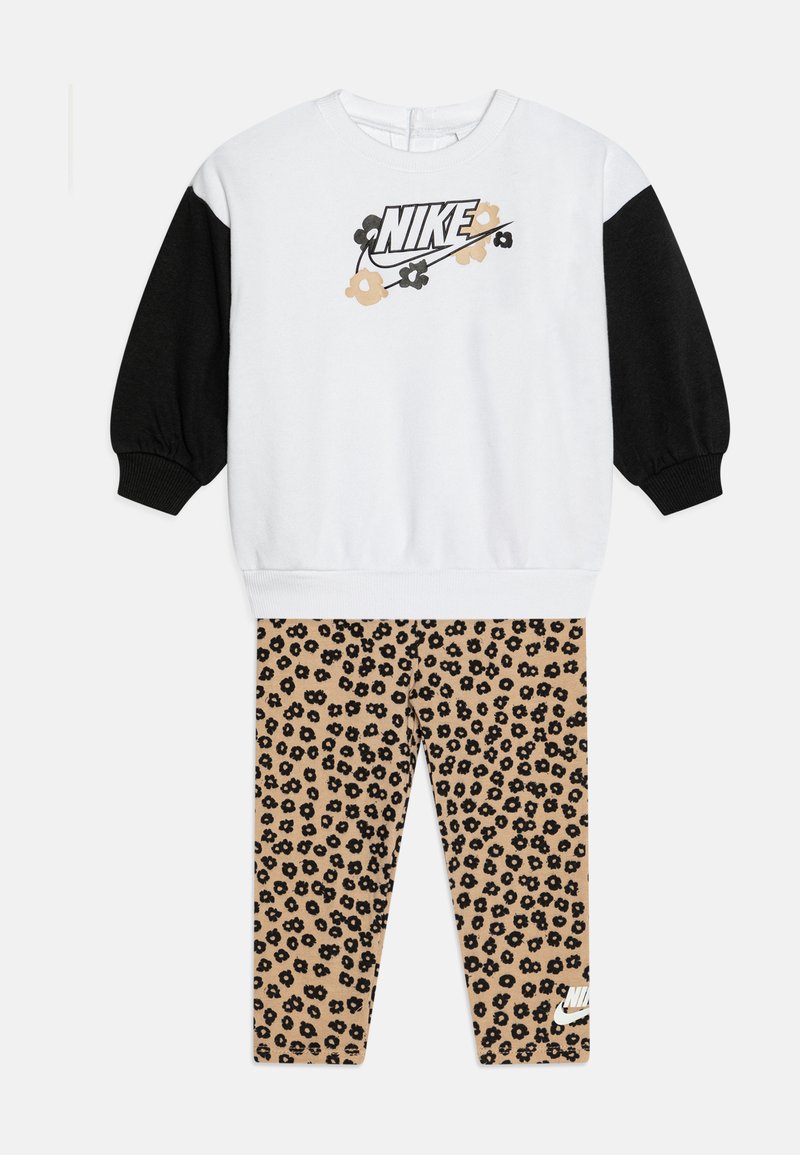 Kleinkind-Outfit von Nike mit einem weißen Sweatshirt, das schwarze Ärmel und ein florales Logo aufweist, kombiniert mit beigen Leggings mit schwarzem Blumenmuster und kleinem Logo.