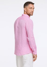 Camicia di lino rosa con colletto, maniche lunghe e polsini a bottoni. Presenta una vestibilità comoda con un orlo leggermente curvo e un tessuto testurizzato.