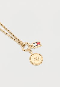 Χρυσή αλυσίδα με στρογγυλό μενταγιόν που απεικονίζει άγκυρα και το κείμενο "Tommy Hilfiger", και μικρό ορθογώνιο γούρι με σημαία.