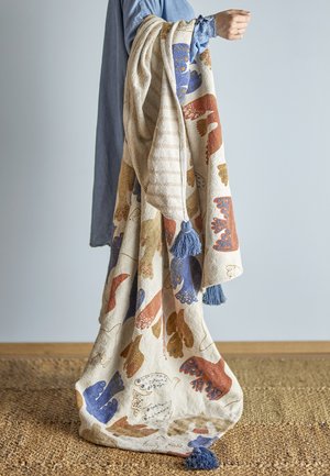 Couverture tissée avec des motifs de feuilles colorées en rouille, bleu et crème. Finition avec des pampilles bleues aux coins. Texture douce.