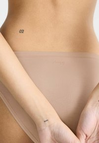 Beige Slip mit glatter Textur und einfachem Design. Verfügt über dezente Markenkennzeichnung und einen niedrigen Schnitt, geeignet für den alltäglichen Gebrauch.