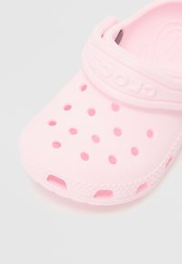 Pink rubber clogs with ventilation holes, a textured surface, and a soft strap featuring the "CROCS" logo on the upper.