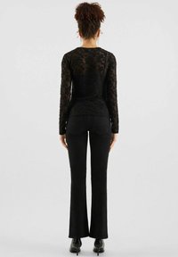 Schwarzes langärmeliges Spitzenoberteil mit floralem Muster, kombiniert mit eng anliegenden schwarzen Schlagjeans. Glatte Textur, taillierte Silhouette und minimalistische Details.