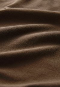 Brauner Baumwollstoff mit glatter Textur, der subtile Falten und ein weiches, mattes Finish aufweist. Ideal für verschiedene textile Anwendungen.