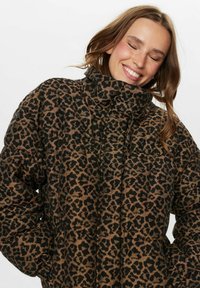 Puhasti z leopardjim vzorcem z visokim ovratnikom in zoženimi manšetami. Material je našit z sijočim zaključkom v zemeljskih tonih.