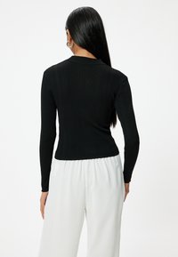 Schwarzes, geripptes Langarmoberteil mit figurbetontem Design und Rundhalsausschnitt, kombiniert mit weit geschnittenen weißen Hosen.