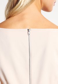 Robe rose clair avec un décolleté dénudé, dotée d'une fermeture éclair en métal dissimulée à l'arrière et d'une texture de tissu lisse.