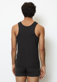 Camiseta sin mangas negra de tela acanalada, con escote redondo y bordes limpios, combinada con pantalones cortos oscuros a juego.