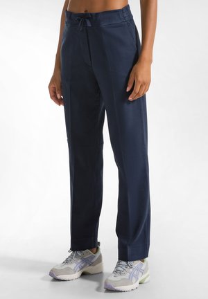 Marineblauwe, lichte, elastische broek met een drawstring, met een relaxte pasvorm en een subtiele glans, gecombineerd met grijze sportschoenen.