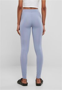 Lys blå leggings med en glatt tekstur, høy midje og tettsittende design, sammen med mørke slip-on sandaler.