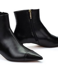 Botas de cuero negras hasta el tobillo con punta afilada, que cuentan con un cierre lateral con herrajes dorados y una textura suave y elegante.
