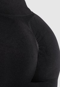 Gros plan sur un tissu noir extensible formant un vêtement arrondi et rembourré, probablement conçu pour l'amélioration ou le soutien du corps.