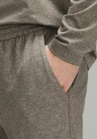 Ruskea, textured-henkaiset jogging-housut, joissa on elastinen vyötärö ja sivutaskut; tiukat hihansuut ja lahkeet.